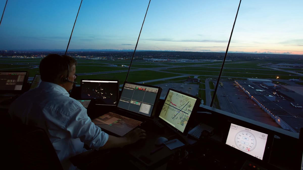 An air traffic controller working radar and airfield displays in a tower cab at dusk