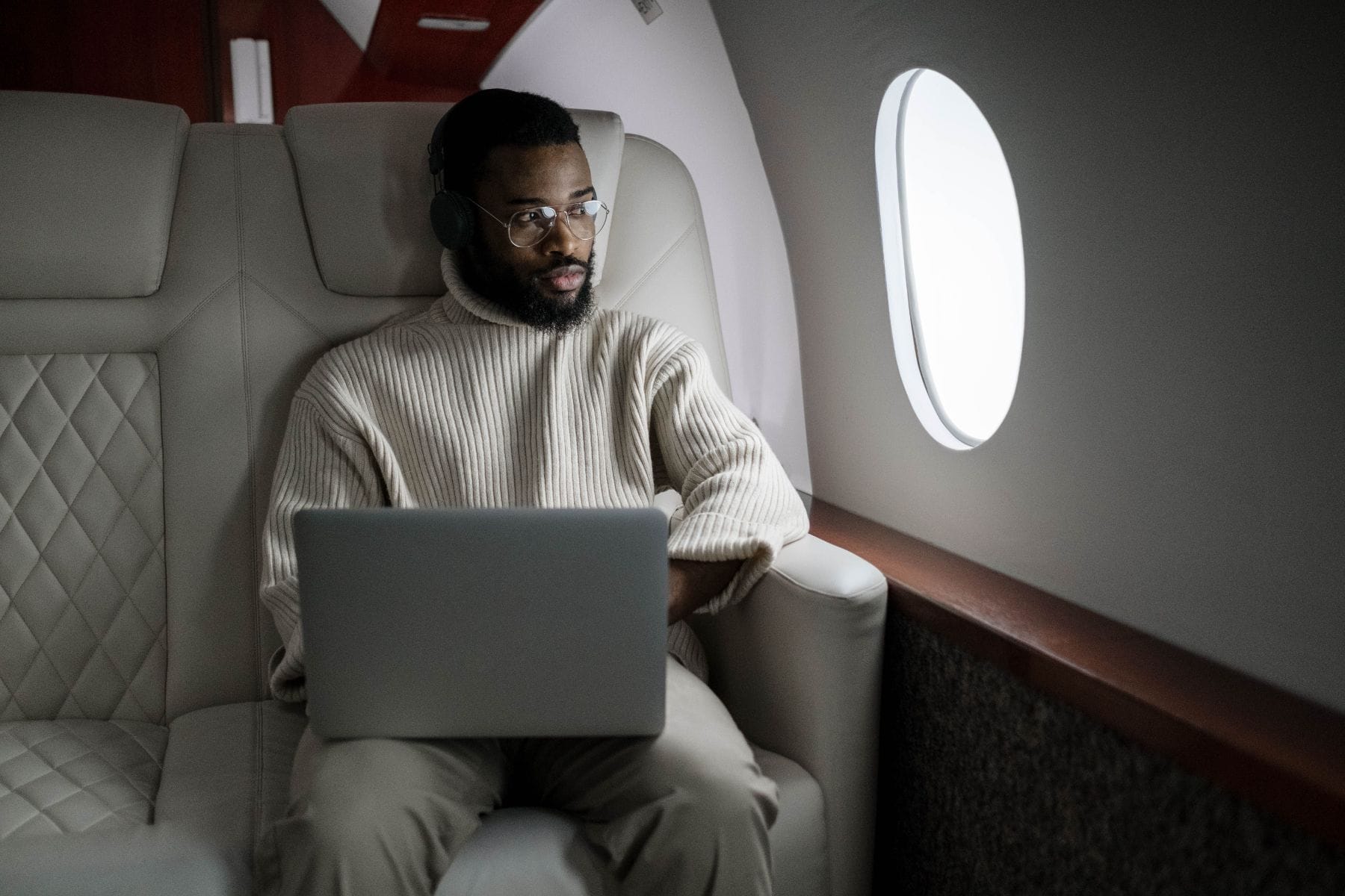 A traveler working on a laptop in a private jet cabin beside the window