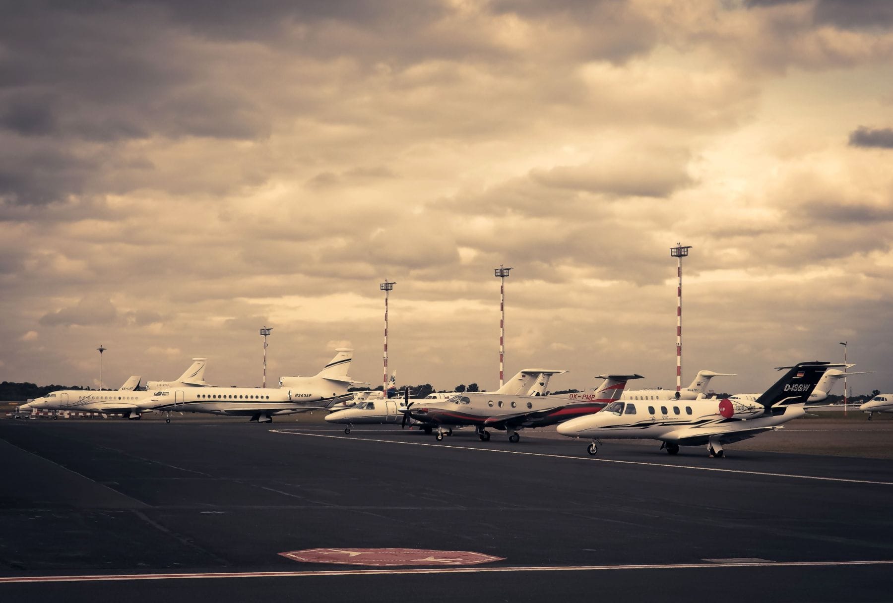 A line of private jets parked on an airport ramp under overcast skies