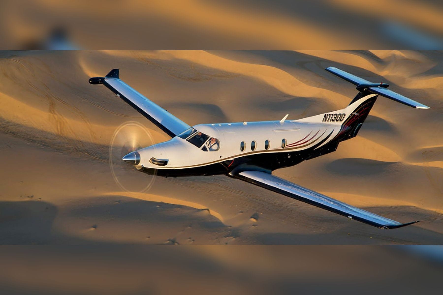 A Pilatus PC-12 turboprop in flight above desert dunes at golden hour