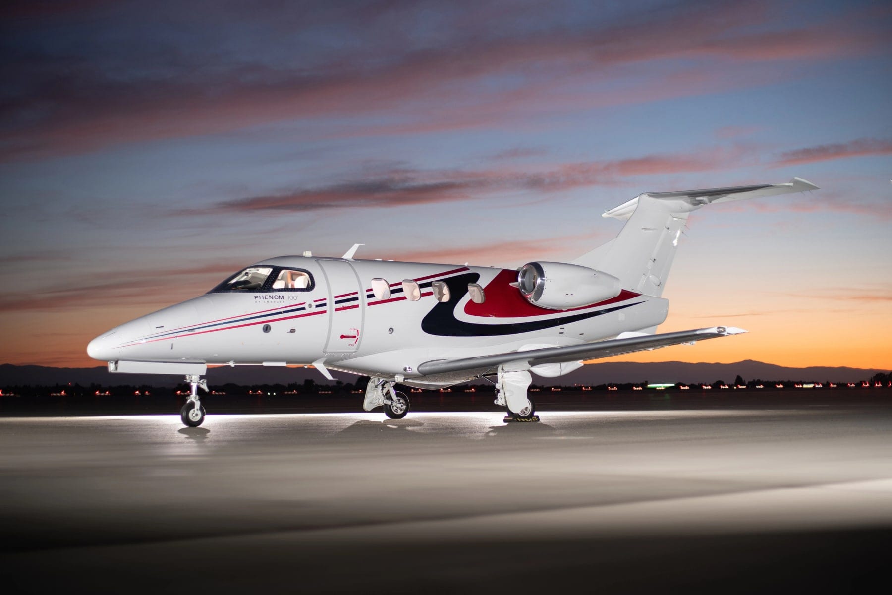 An Embraer Phenom 100 very light jet parked on the ramp at dusk